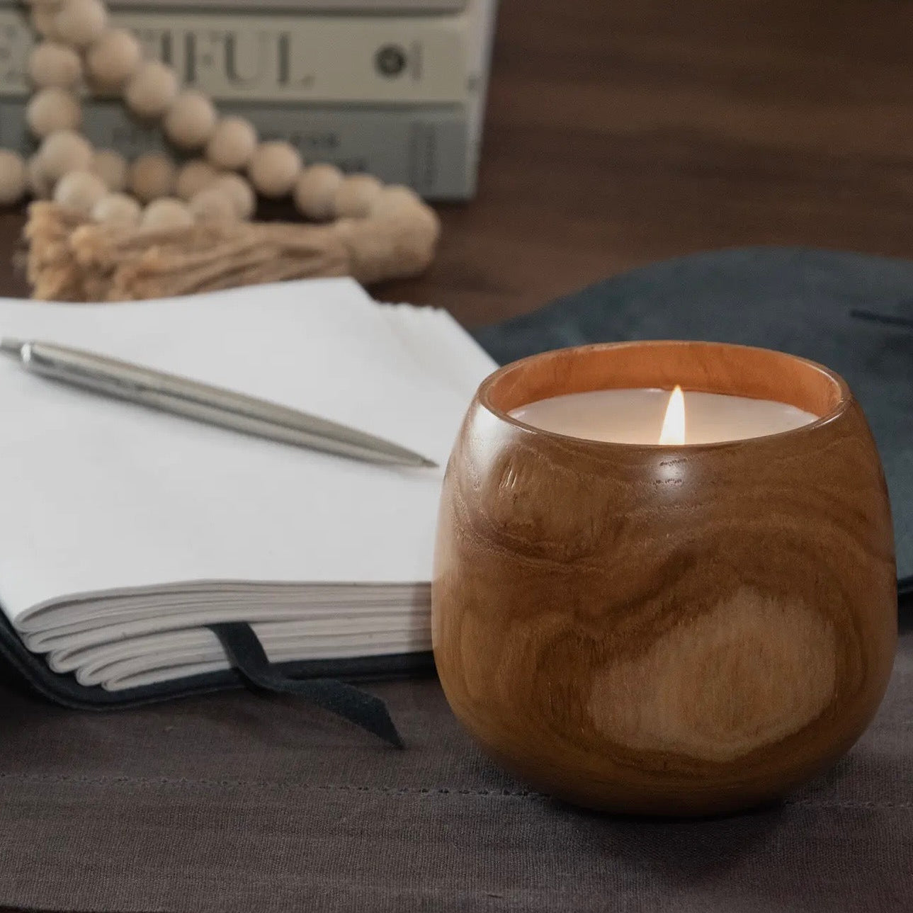 Wooden candle holder with a lit candle on a table with a notebook and pen.