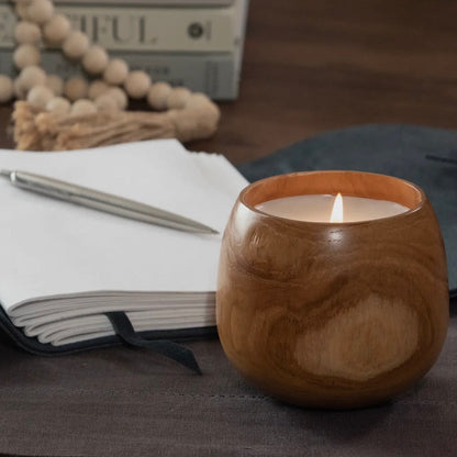 Wooden candle holder with a lit candle on a table with a notebook and pen.