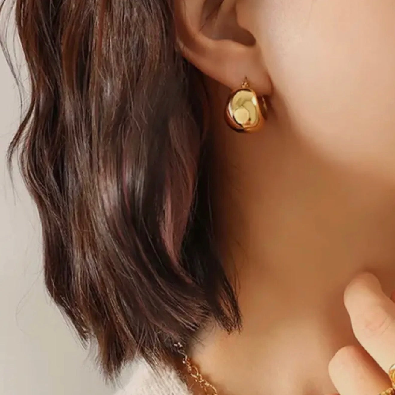 Close-up of a person wearing a gold earring with a green gemstone.