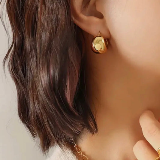 Close-up of a person wearing a gold earring with a green gemstone.