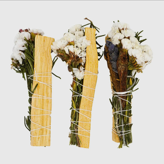 Three bundles of dried herbs and flowers tied together with twine on a white background