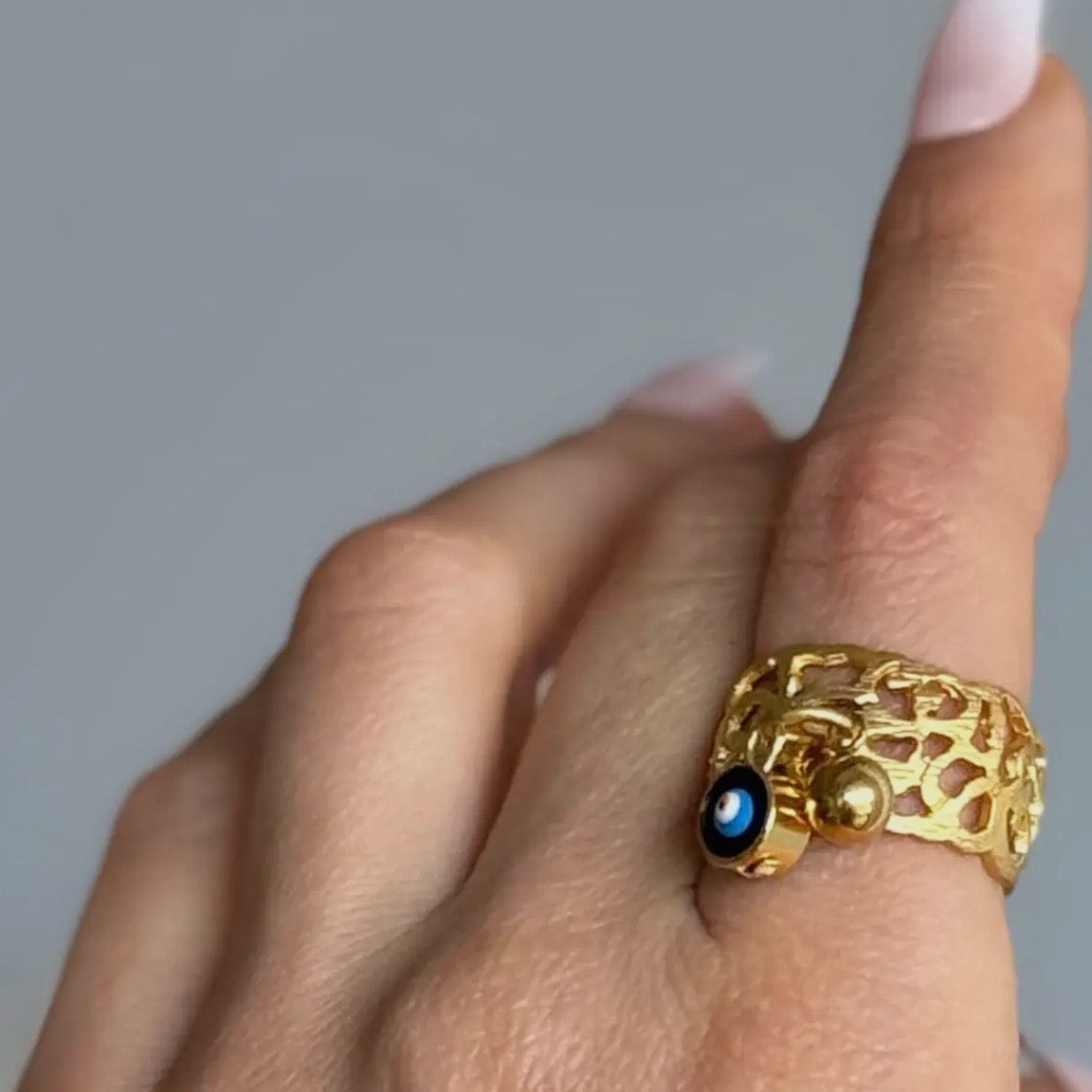 Gold ring with a blue gemstone on a finger against a gray background