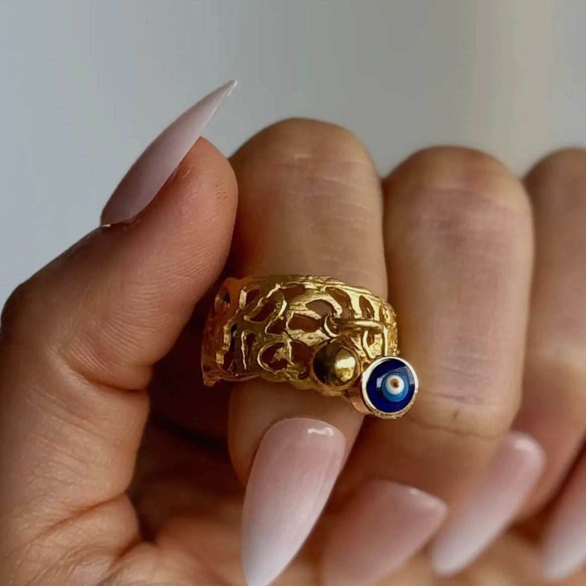 Gold ring with blue stone held by a hand against a neutral background